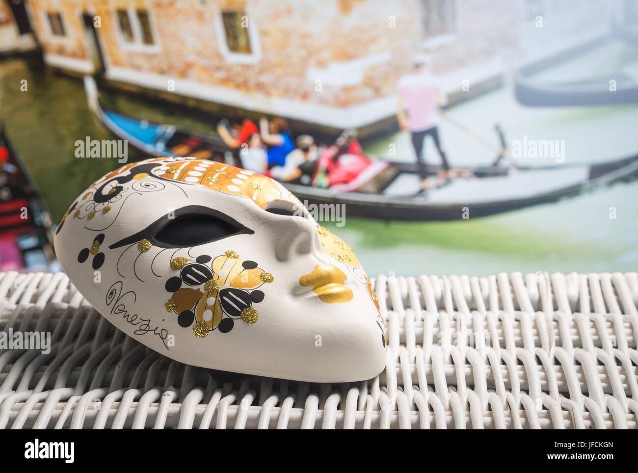 Authentic mask from Venice with a gondolier and tourists in gondola in the background. Golden souvenir and traditional Venetian boat in the canal. Stock Photo