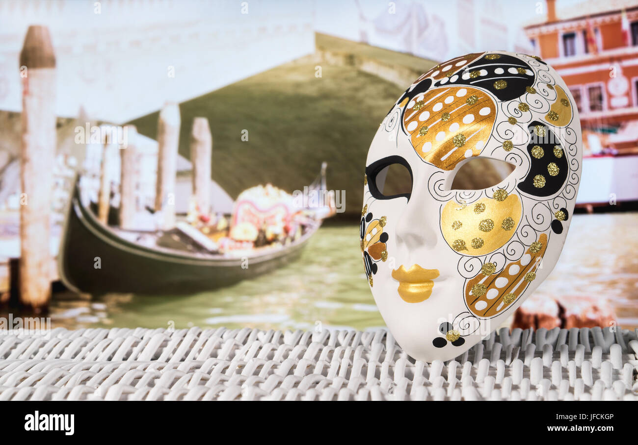Mask from Venice with a gondola moored by Rialto Bridge. Golden and decorative souvenir and a traditional Venetian boat in the canal. Stock Photo