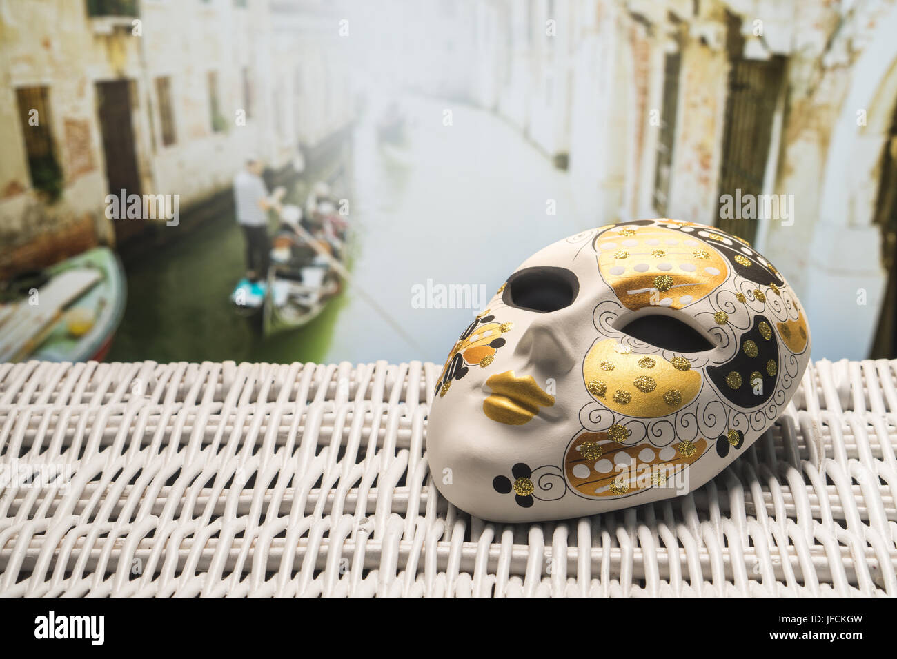 Mask from Venice with a gondolier rowing a gondola in a narrow canal in the blurred background. Golden and ornamental souvenir in Italy. Stock Photo