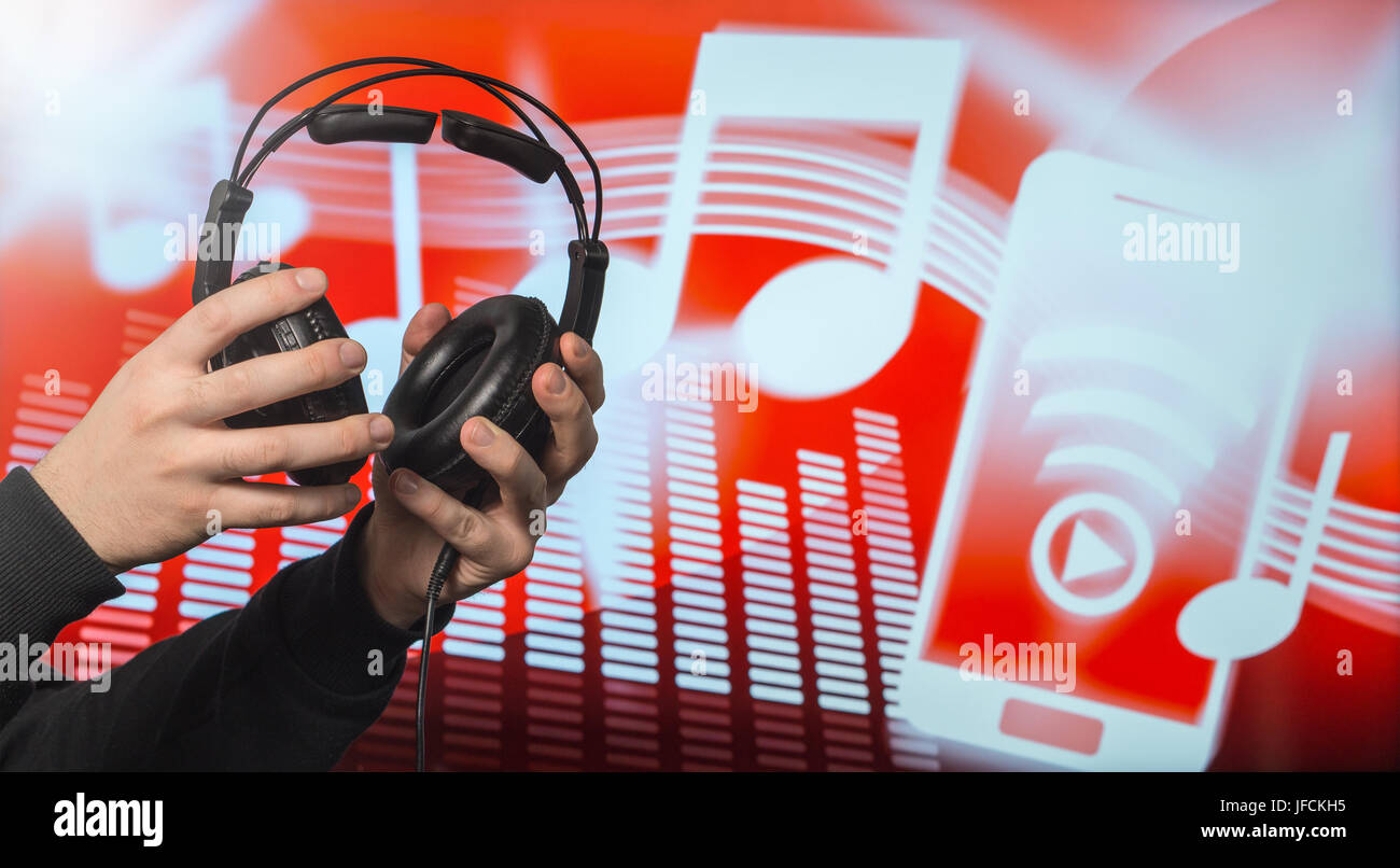 Close up of male hands holding large headphones in front of an abstract note and equalizer background. Man putting earphones on and listen to music. Stock Photo