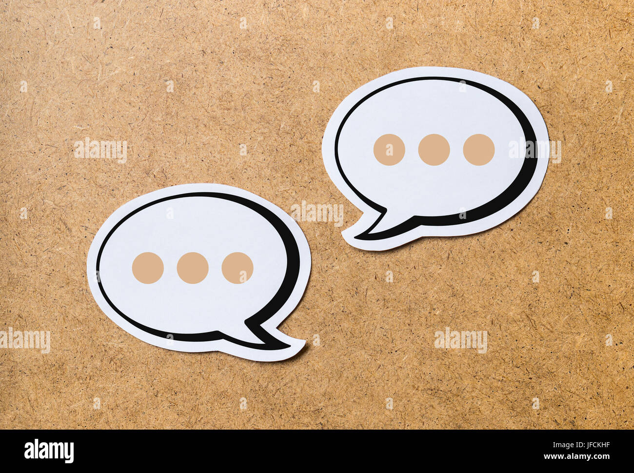2 speech bubbles on a light brown wooden cork board background. Chat bubble and icon cut from paper and cardboard. Discussion, chat and commenting. Stock Photo