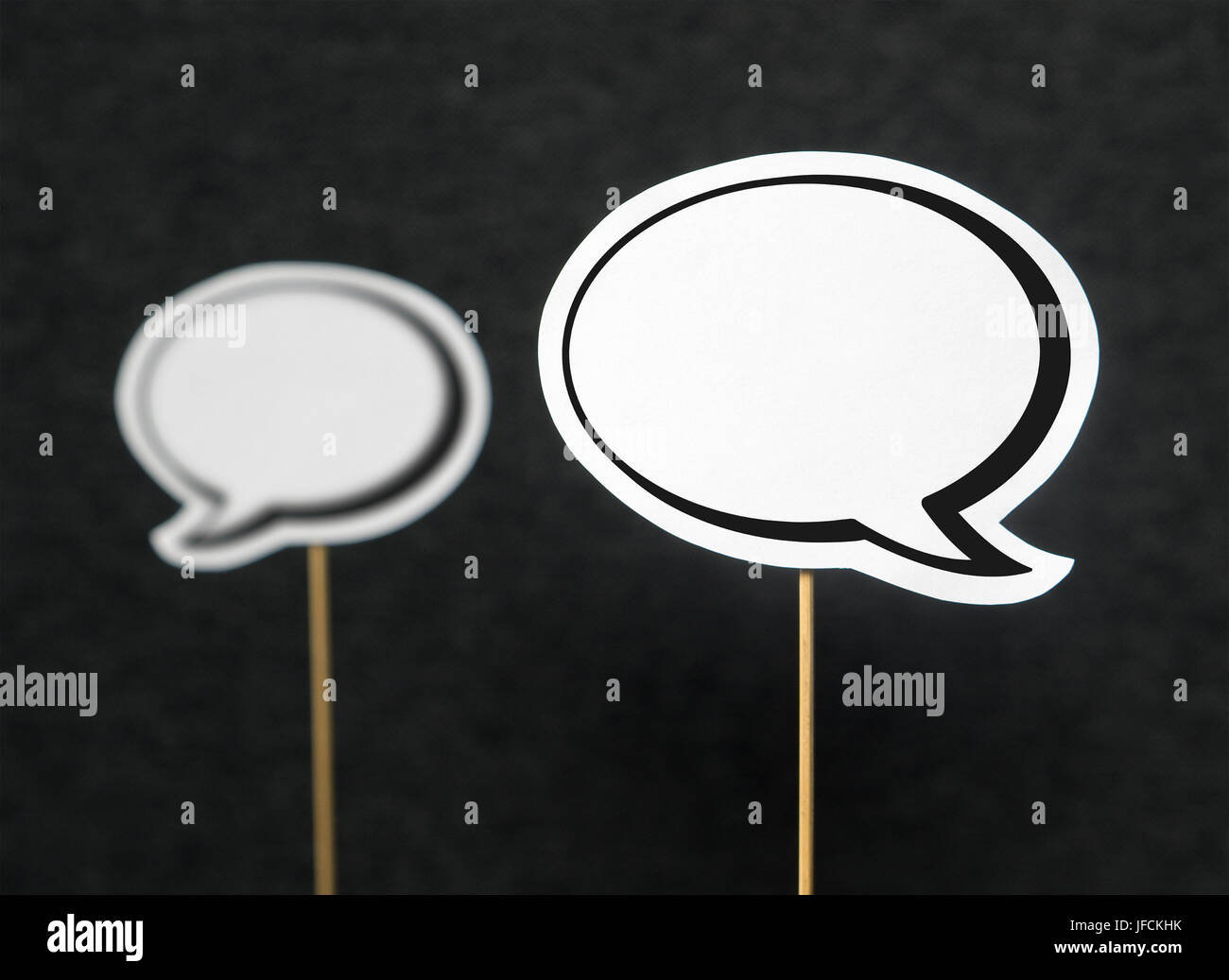 2 blank speech bubbles on a dark black background. The other speech balloon blurred. Chat bubble cut from paper with wooden stick. Discussion, protest Stock Photo
