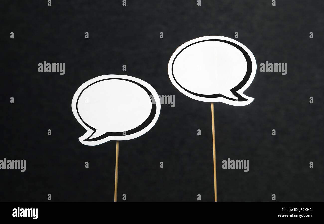 2 blank speech bubbles on a dark black background. Chat bubble cut from paper with wooden stick. Fun discussion, protesting and commenting concept wit Stock Photo