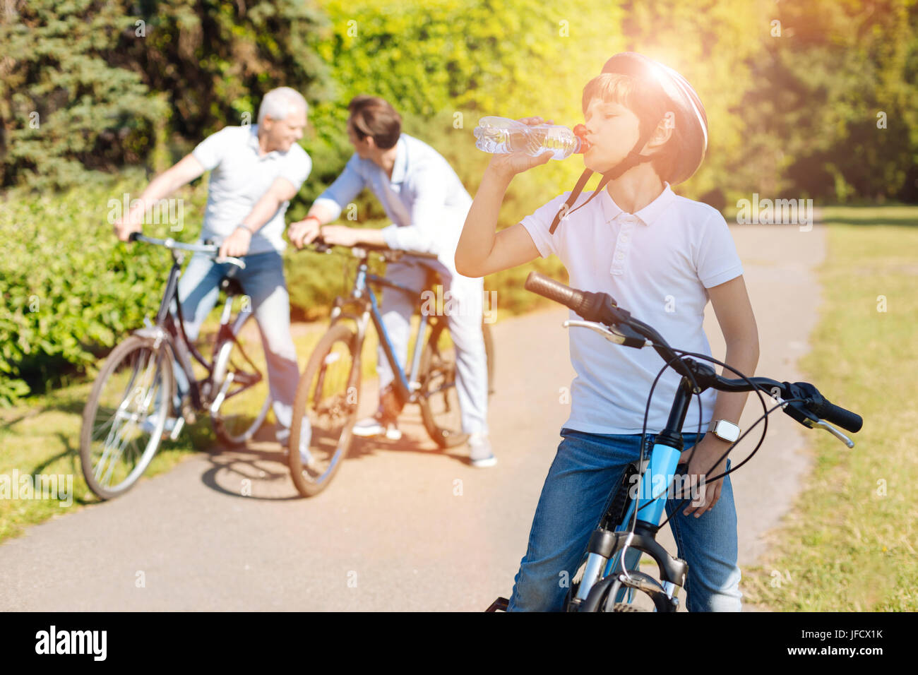 Thirst for adventure. Inspired diligent bright kid exercising with his family while riding bicycles and feeling thirsty Stock Photo