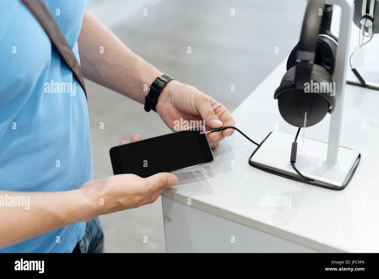 Let me try this out. Scaled up shot of a male customer trying to plug mockup headphones into his smartphone while standing at a display and shopping f Stock Photo