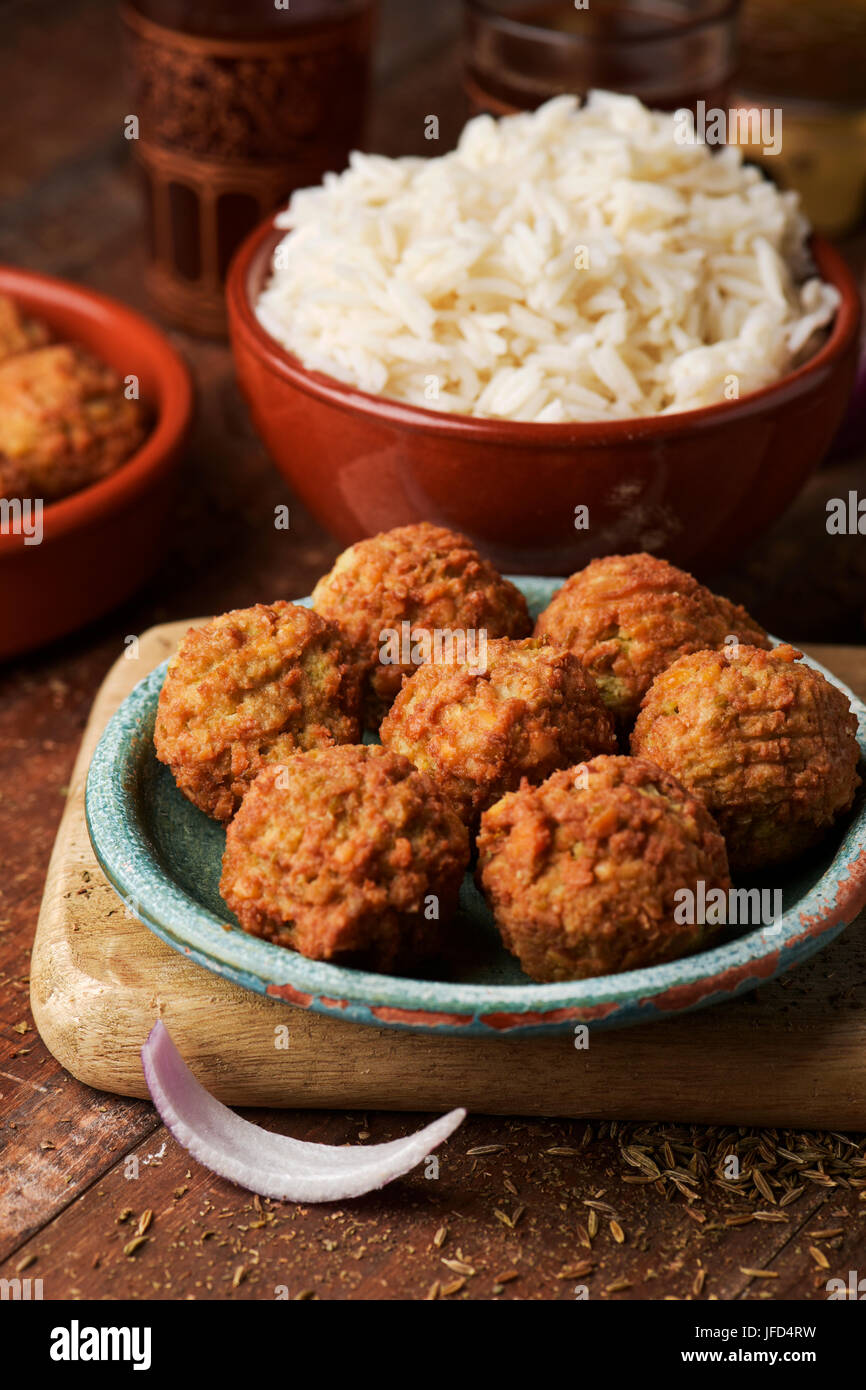 some falafel in a green earthenware plate and a brown earthenware bowl with long grain rice on a rustic wooden table, with some ornamented glasses wit Stock Photo