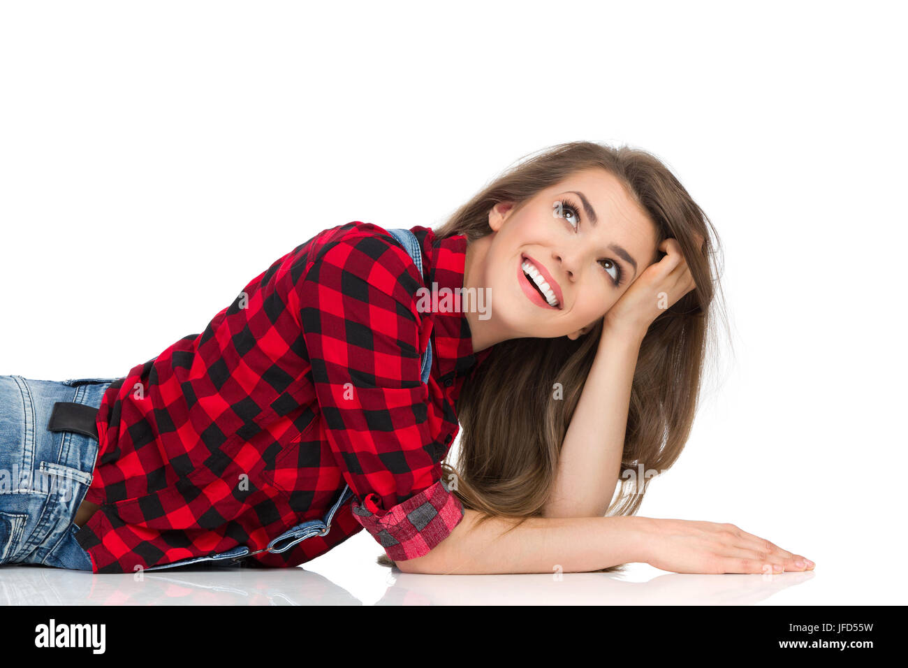Smiling young woman in red lumberjack shirt lying on a floor and looking away. Waist up studio shot isolated on white. Stock Photo