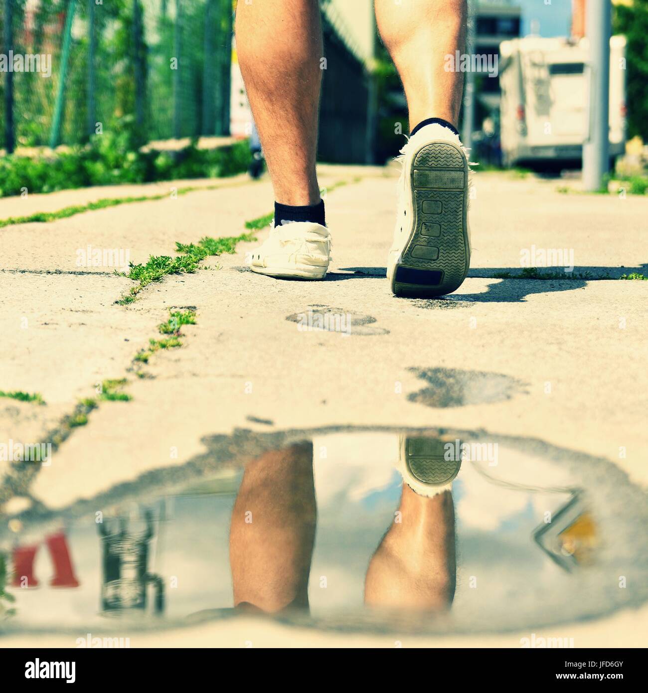 Legs while walking. Reflections in water on the sidewalk. Stock Photo
