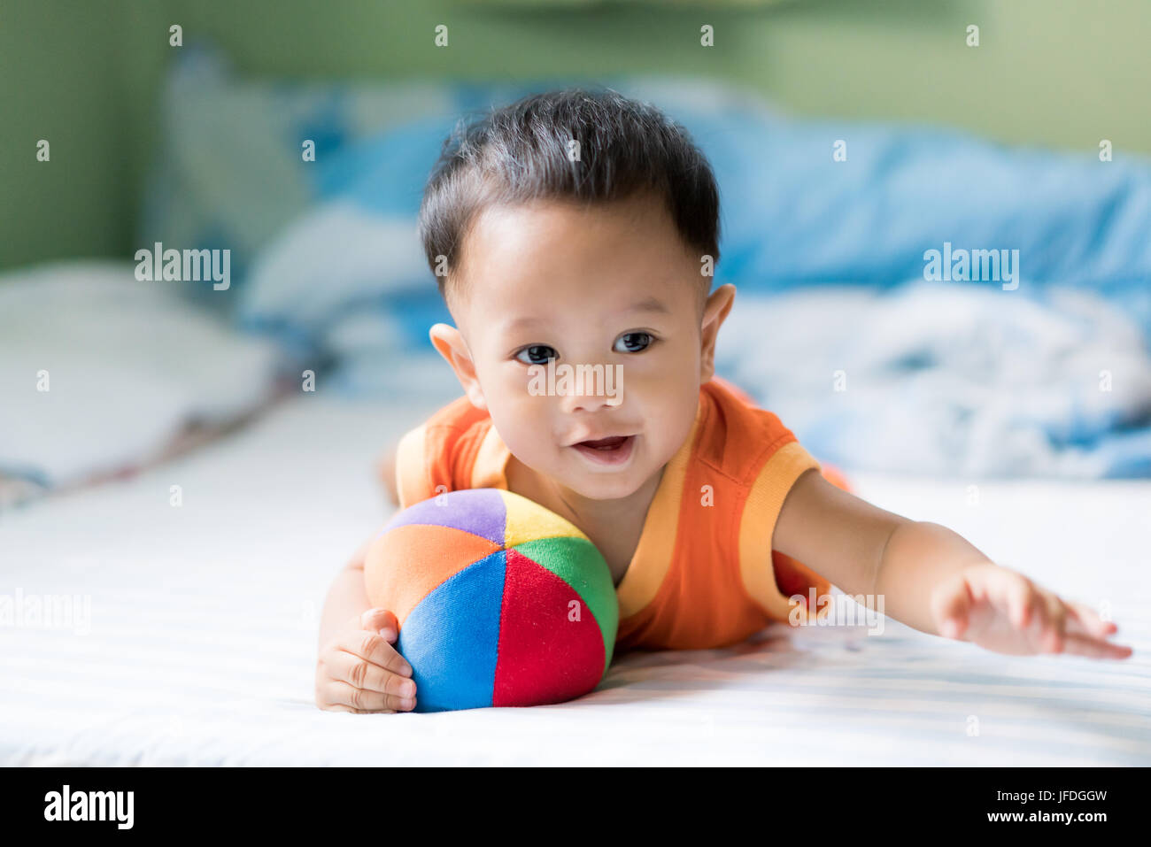 Asian adorable baby boy playing with colorful rainbow ball toy in white sunny bedroom at home. Stock Photo