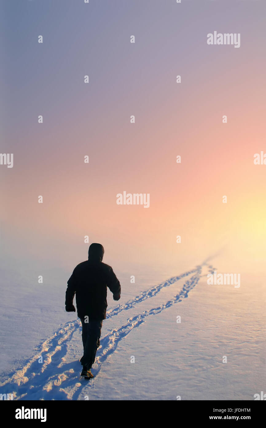 Man walking over the snow alone. There is a beautiful sulight visible in the end of his way. Stock Photo