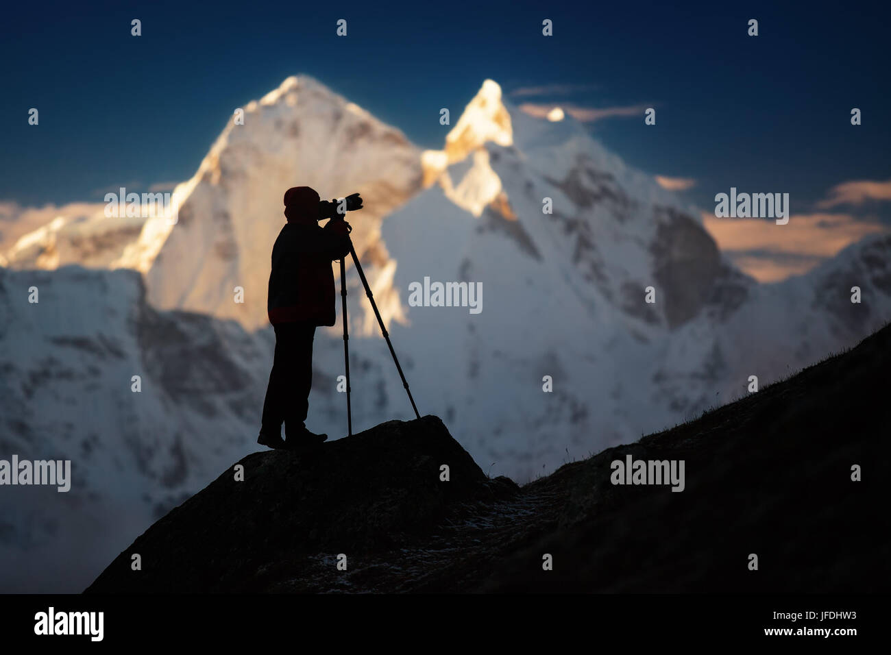 A silhouette of a man (photographer) standing on a hills in front of the mountains. Stock Photo