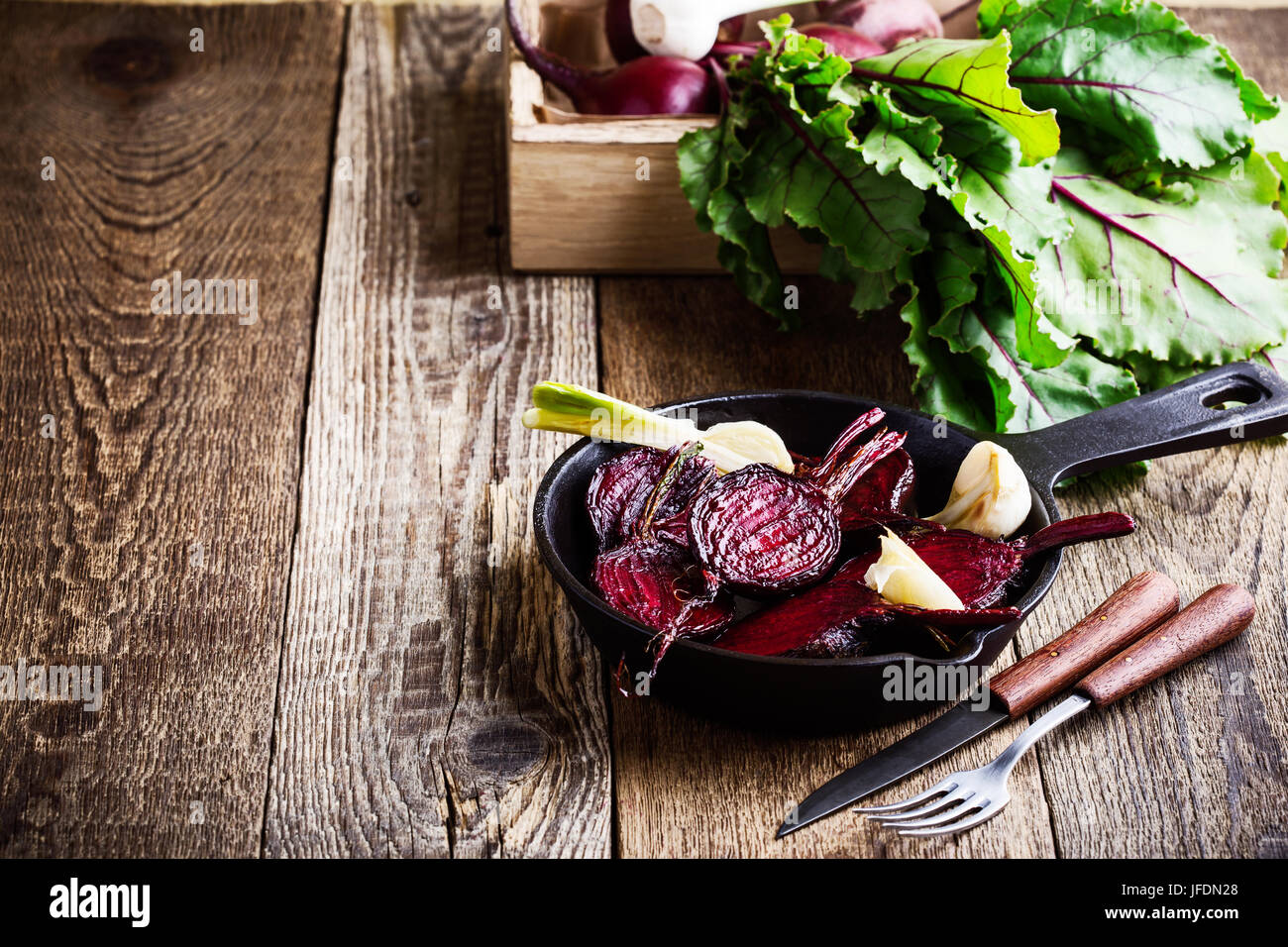 Roasted beetroots in cast iron skillet and fresh vegetables in crate on wooden rustic table Stock Photo