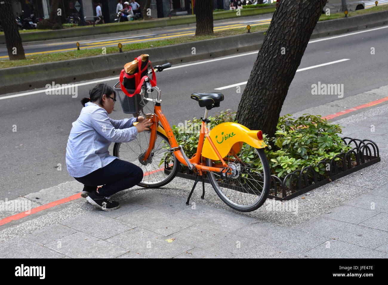 High school student trying to fix the public U bike so she can continue on her way, Taipei, Taiwan. Stock Photo