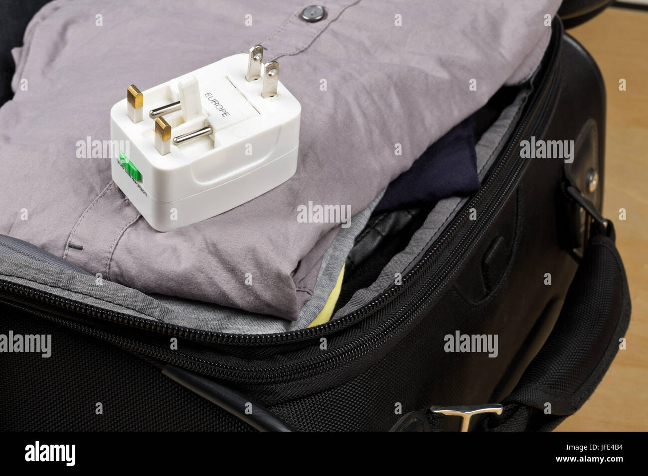 Travel power adapter with connectors for european, UK, and US power plugs on packed suitcase with clothings - travel preparation Stock Photo