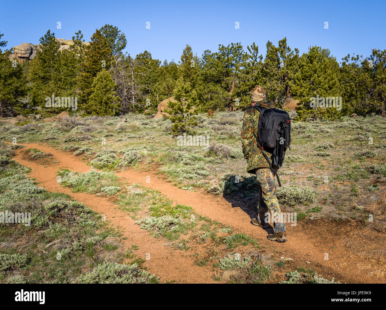A man hiking in camouflage outfit discovering nature in the forest with DSLR photo camera, lenses, tripod in the backpack. Travel photography lifestyl Stock Photo