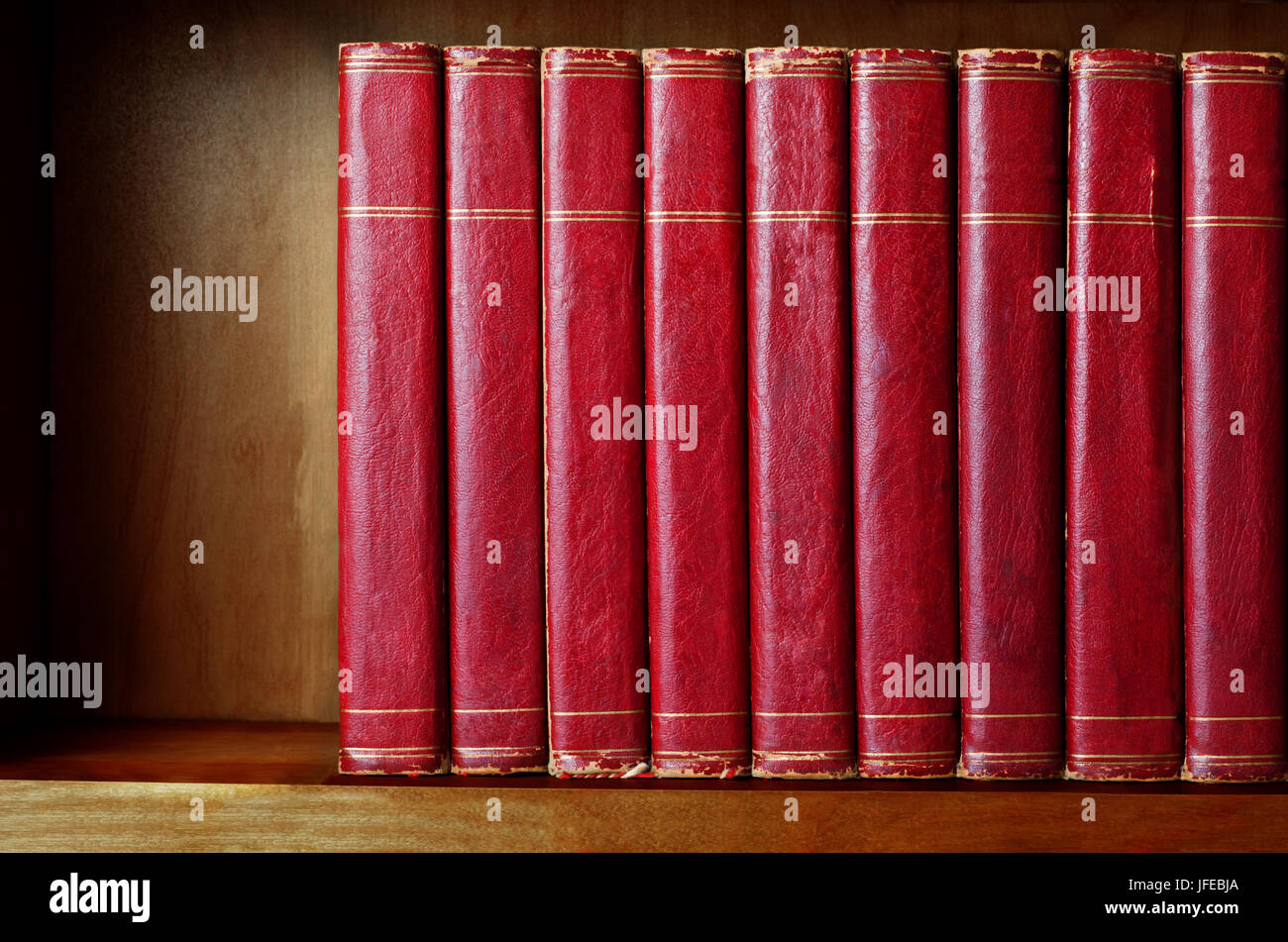 A row of old, battered, matching encyclopaedias (circa 1950s) lined up on a shelf, with titles removed to leave blank spines.  Red leather effect with Stock Photo