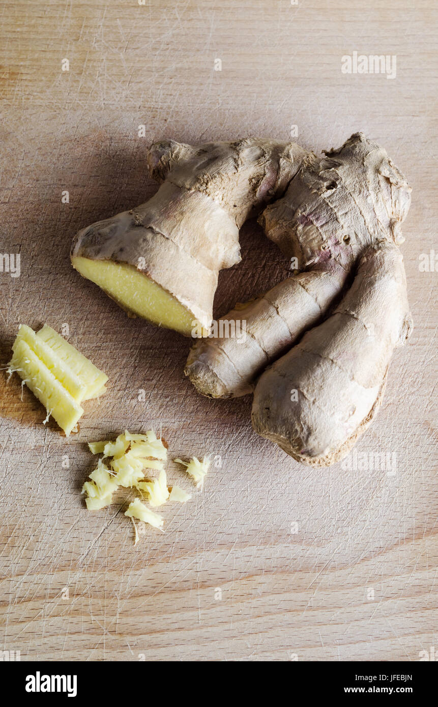 Overhead shot of whole, sliced and roughly chopped ginger root on an old, used  wooden chopping board with many knife cuts on it's surface. Stock Photo