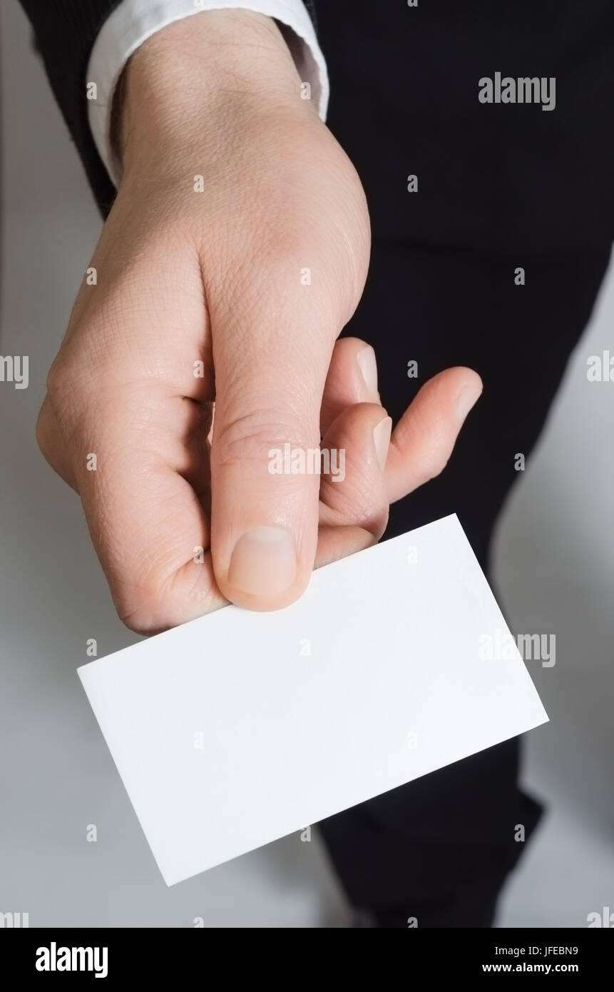 Close up of the hand of a man in a suit, reaching forward holding a blank business card facing upwards towards the viewer. Stock Photo
