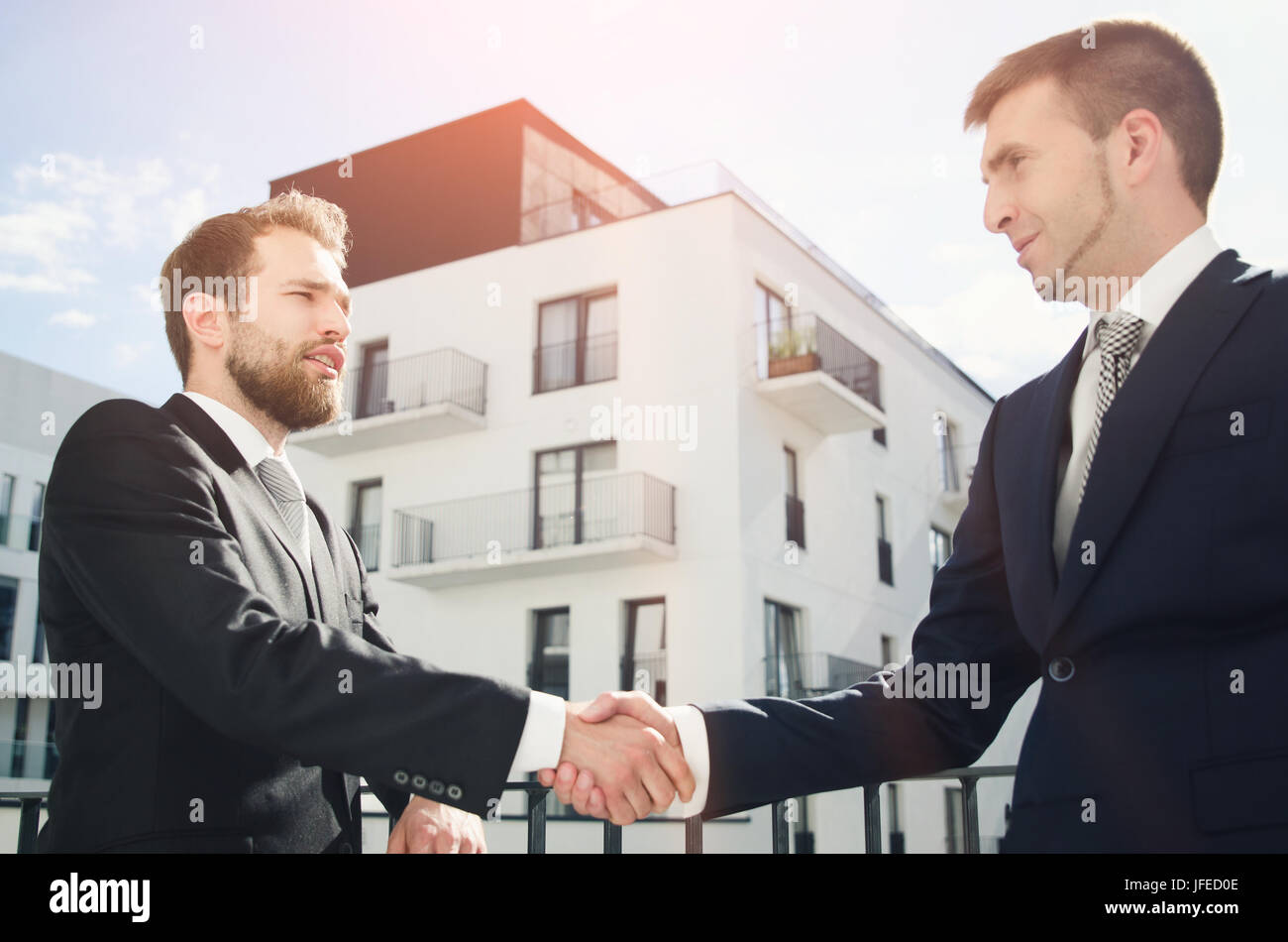 Two men are standing on the balcony and shaking hands. Investor or customer buying apartment Stock Photo