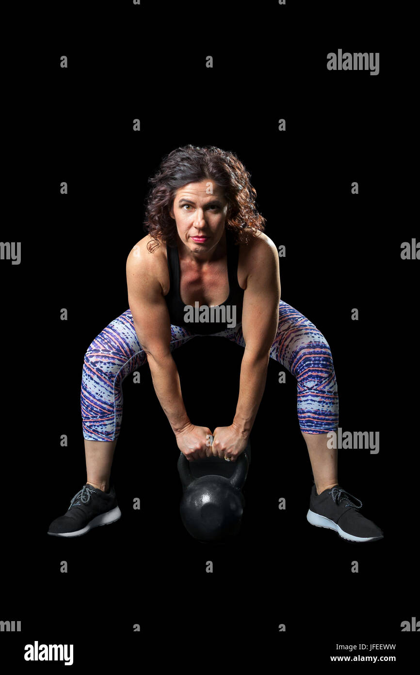 Intense image of a female weightlifter bending over to do a kettlebell dead lift. On a black background.  Path around the woman. Stock Photo