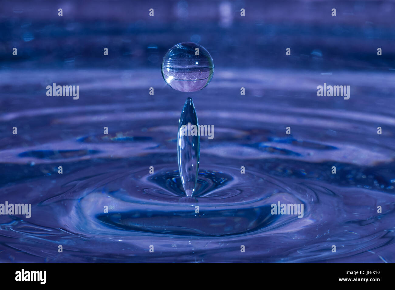 High-speed macro of drop splashing in blue water. Stock Photo