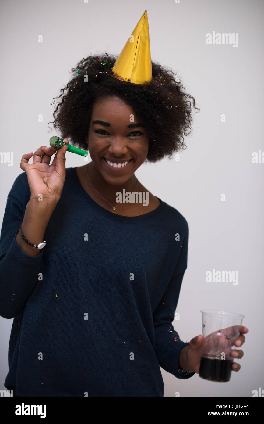portrait of a young beautiful black woman in party hat blowing in ...