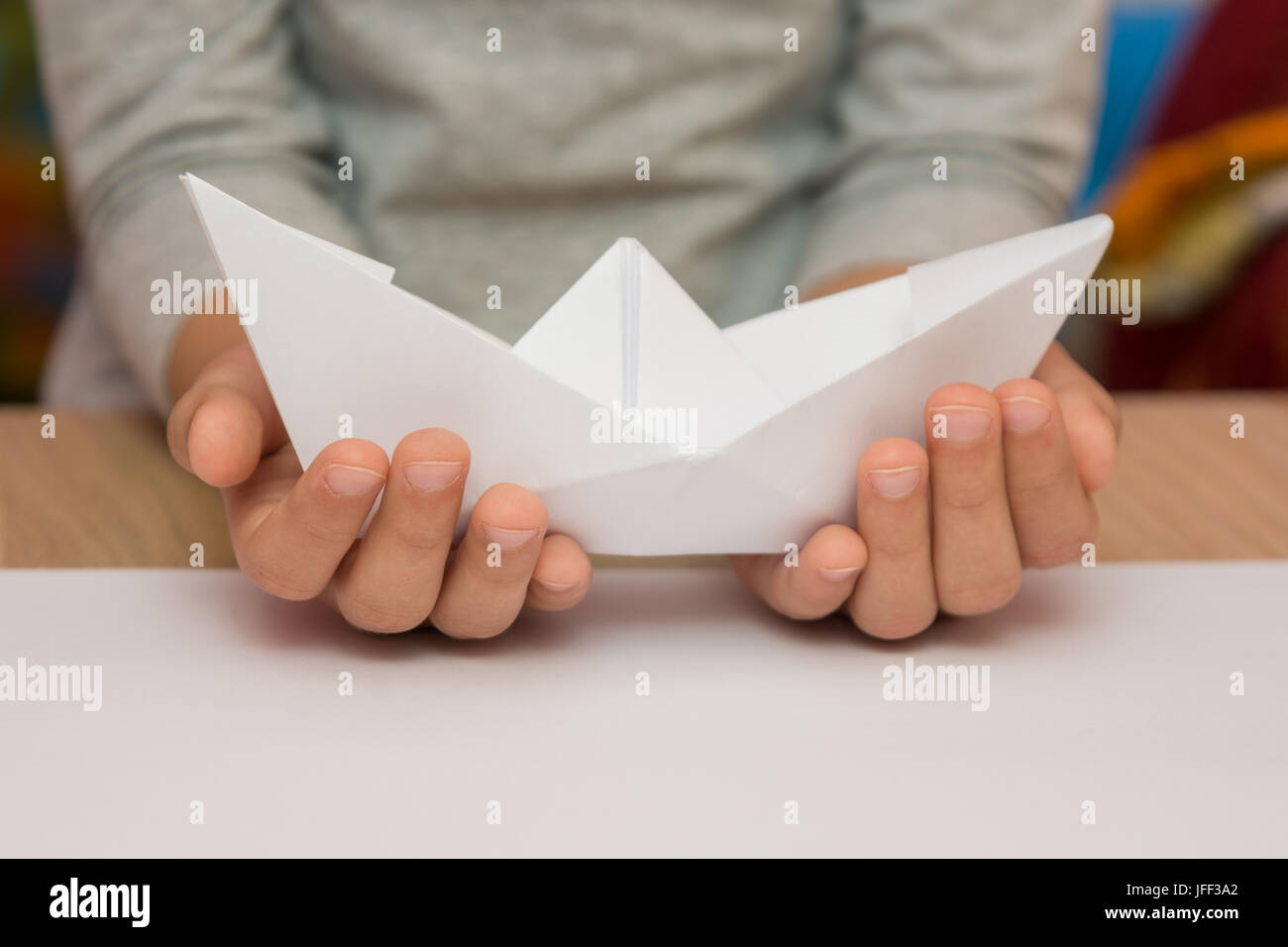 A child holding a white boat made of paper Stock Photo