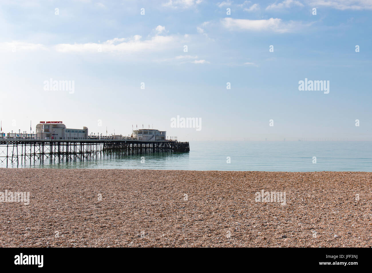 Worthing Pier on a Bright Summers morning with the shingle Beach in the Foreground.  The Sea is Calm and the Sky Blue With a Small amount of Cloud. Stock Photo