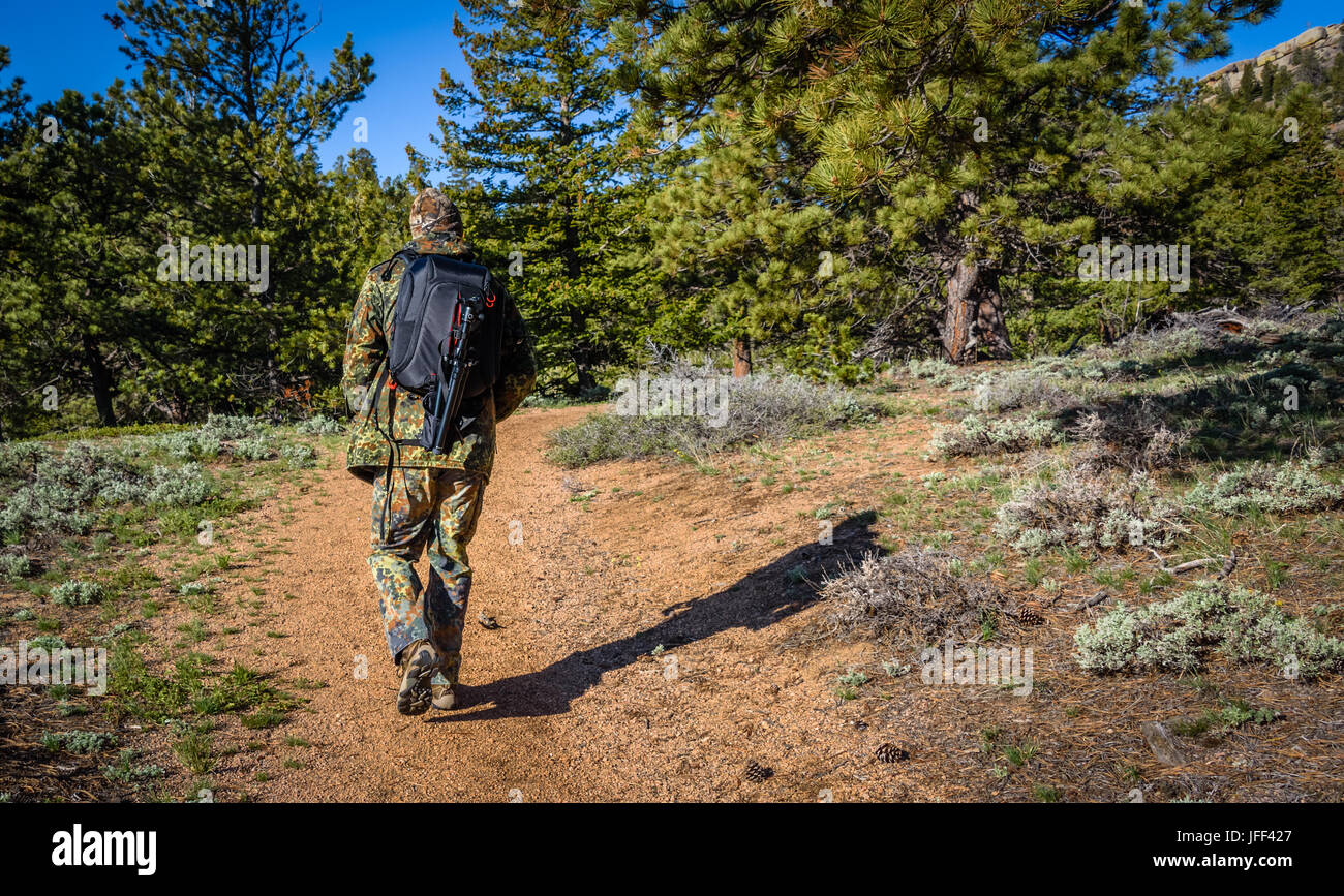 A man photographer hiking in camouflage outfit discovering nature in the forest with DSLR photo camera, lenses, tripod in the backpack. Travel photogr Stock Photo