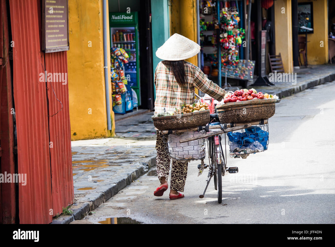 Woman fruit vendor wearing a traditional hat, walking her bicycle, Hoi An, Vietnam Stock Photo