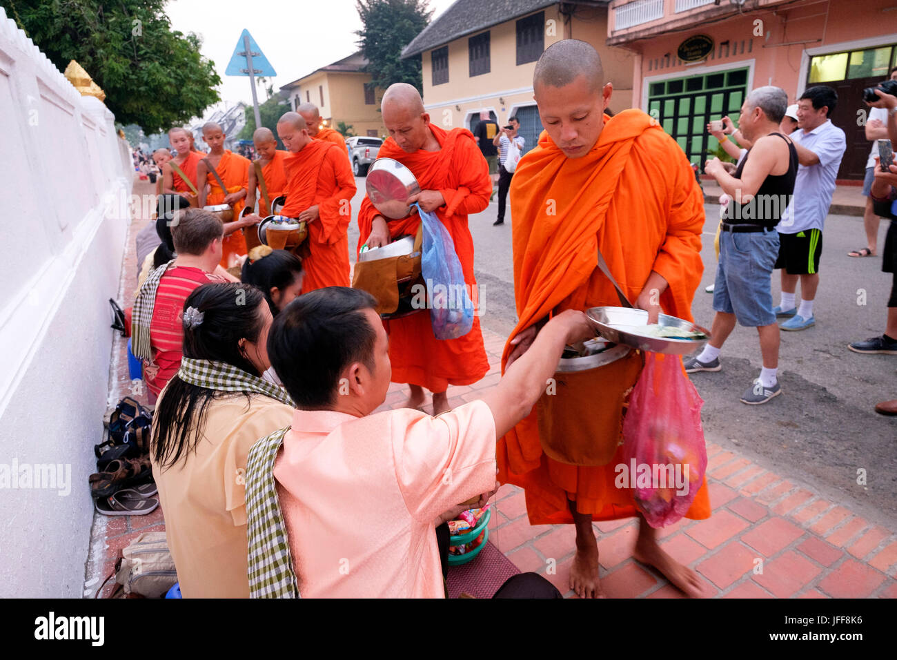 Procession of Buddhist monks wearing orange robes at dawn to collect