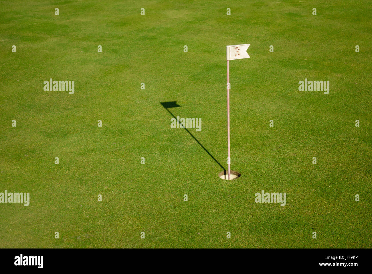 Glof flag mark in hole throwing shadow on the green course grass, golf playing concept Stock Photo