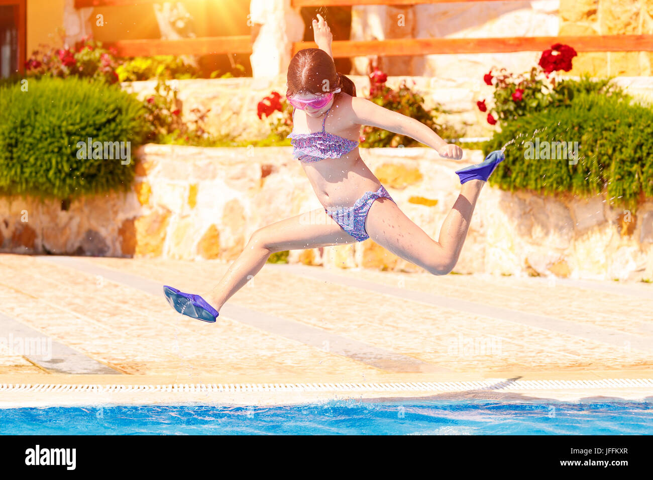 Joyful girl jumping to the pool, cute little child wearing goggles and flippers for diving, happy carefree childhood, enjoying summer holidays on the  Stock Photo