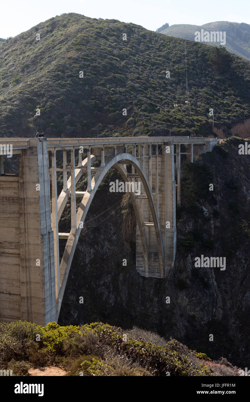 Several people sitting and sightseeing atop the Bixby Creek Bridge, a concrete, open-spandrel arch bridge, on the Pacific Coast Highway. Stock Photo