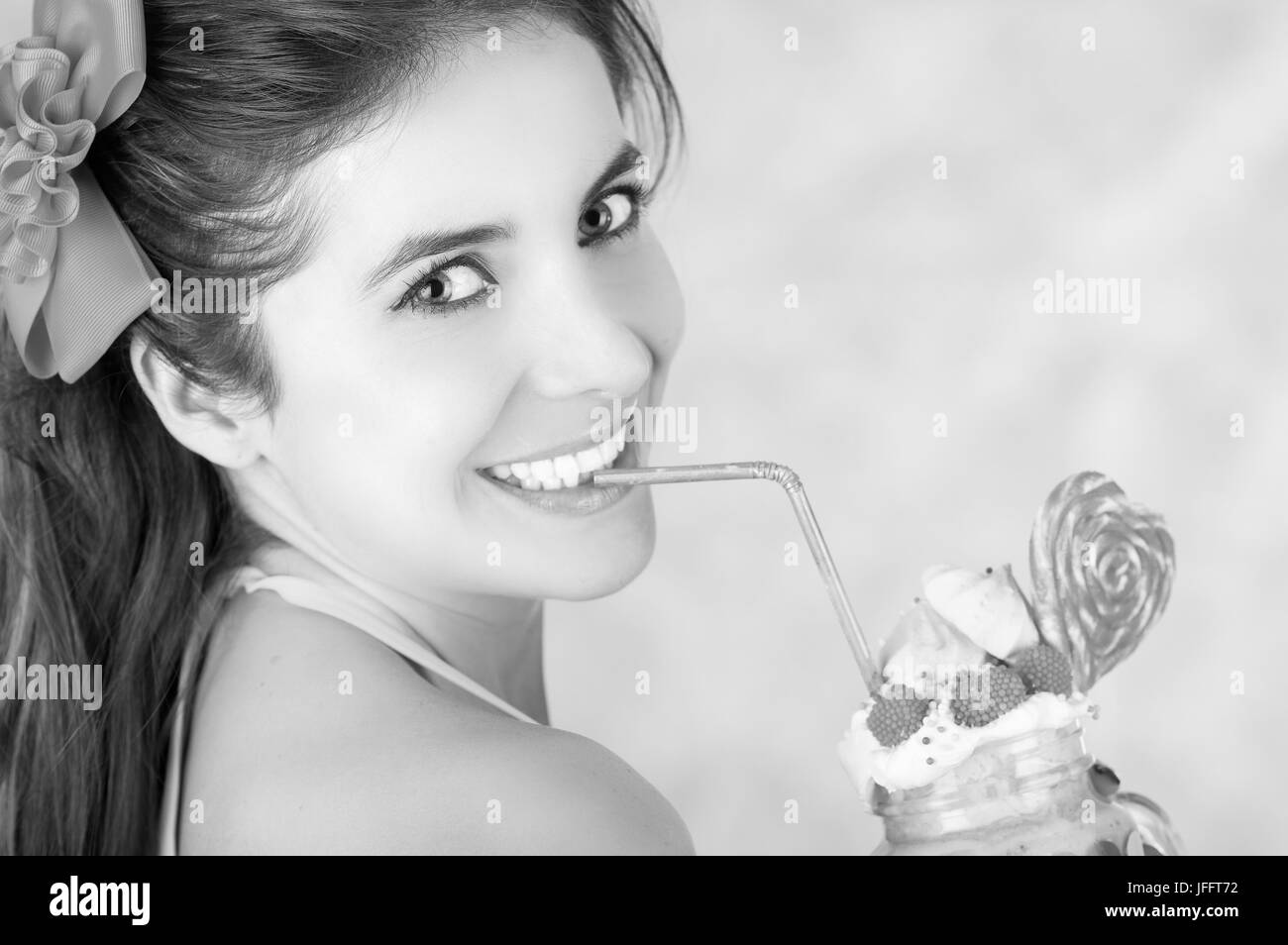 Smiling woman, wearing a pink suitcase, holding a tasty blue milk shake in a jar, with a heart candy, plastic straw on a milk foam on top, in a pink b Stock Photo