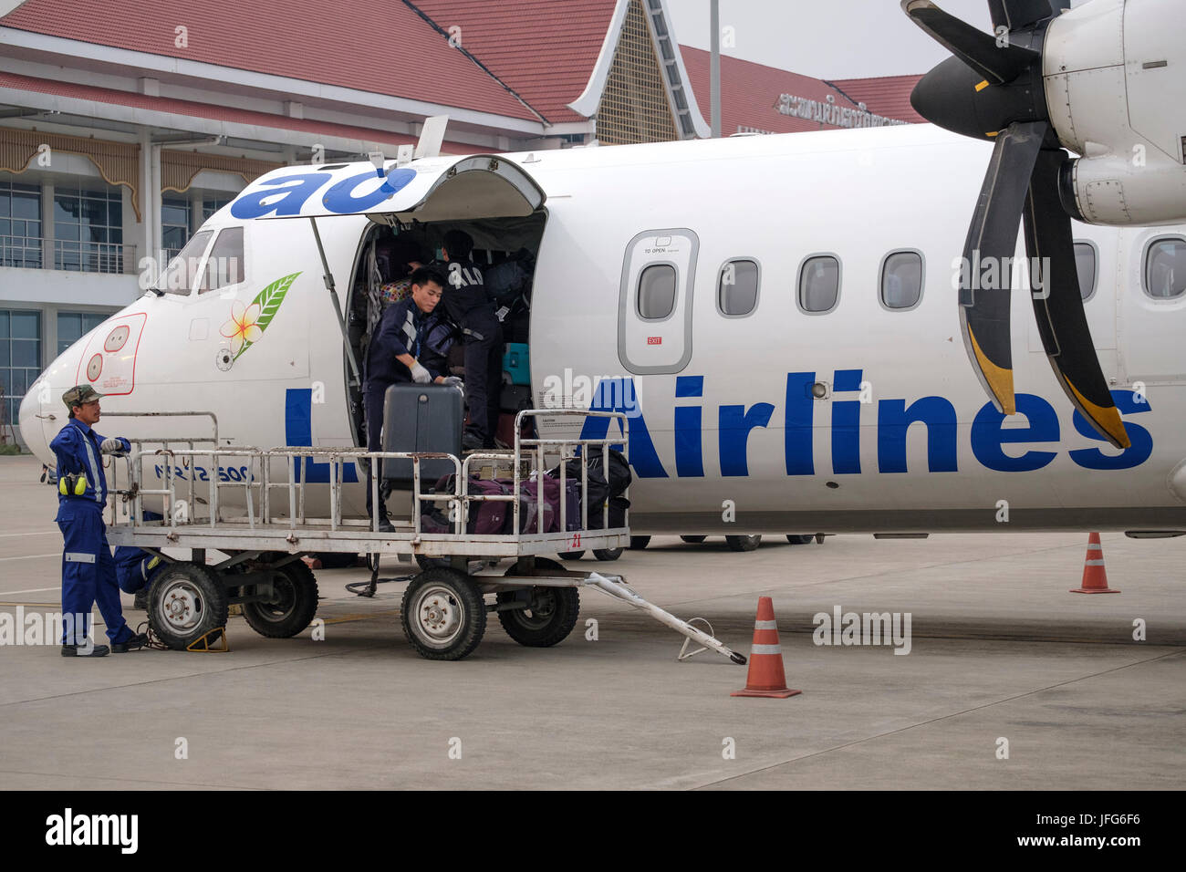 Bag handlers loading luggage into Lao Airlines airplane at airport tarmac Stock Photo