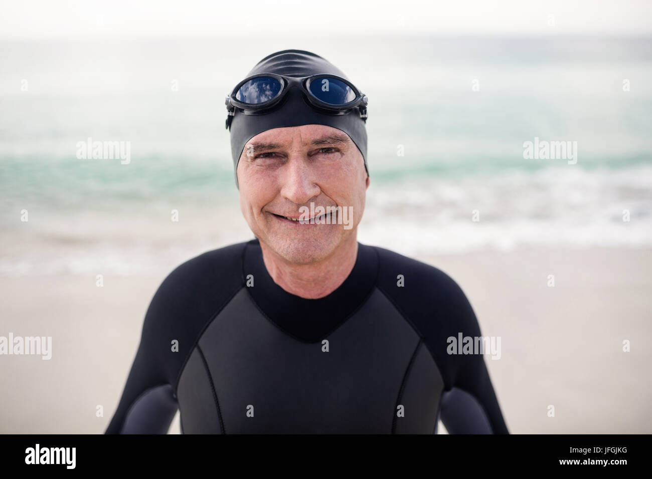 Senior man in wetsuit and swimming goggles standing on beach Stock Photo