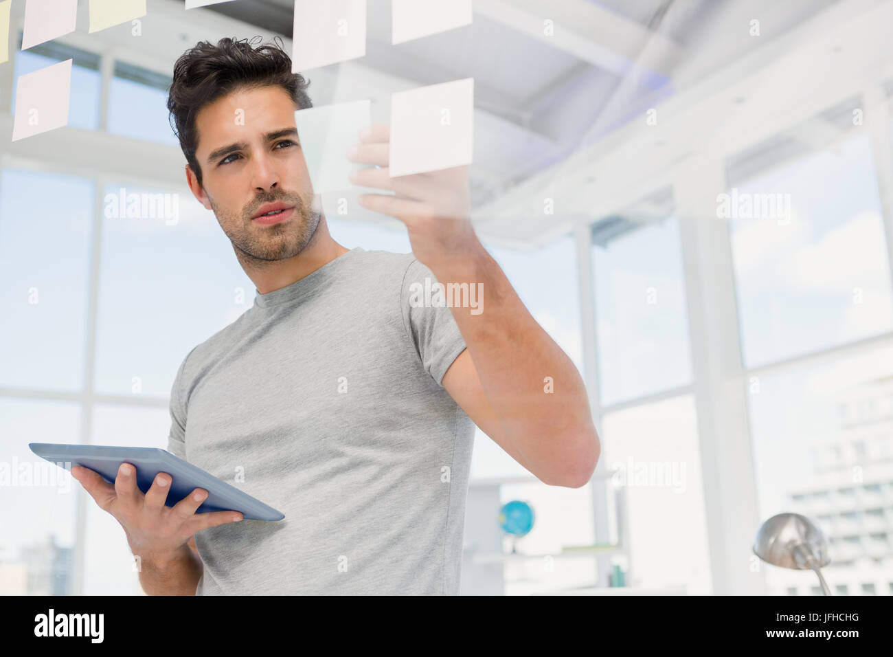 Man holding digital tablet and looking at sticky notes Stock Photo