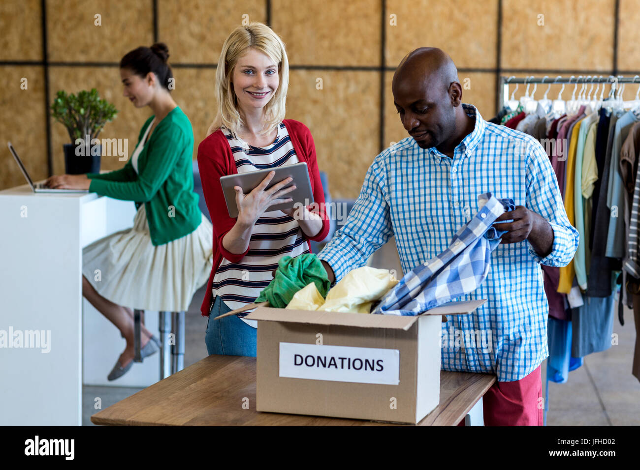 Colleagues using digital tablet while sorting clothes from donation box Stock Photo