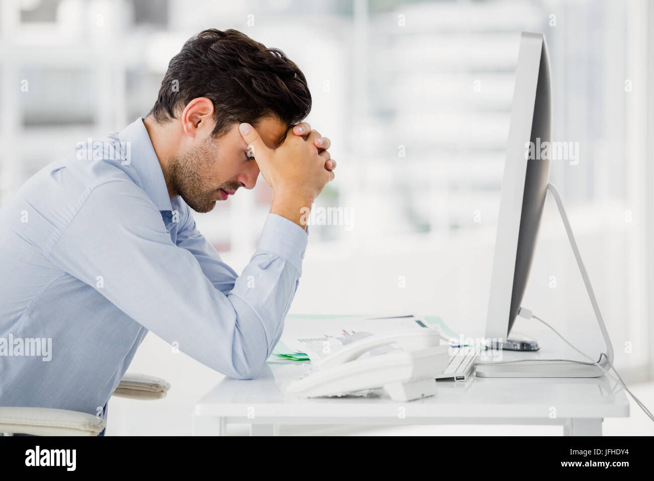 Frustrated businessman sitting on desk with hand on head Stock Photo