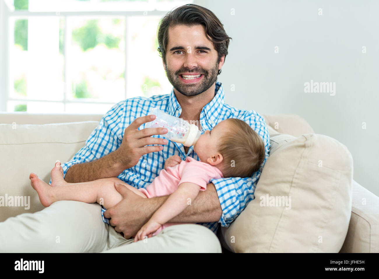 Boy feeding milk to brother from baby bottle while sitting on sofa at home  Stock Photo - Alamy