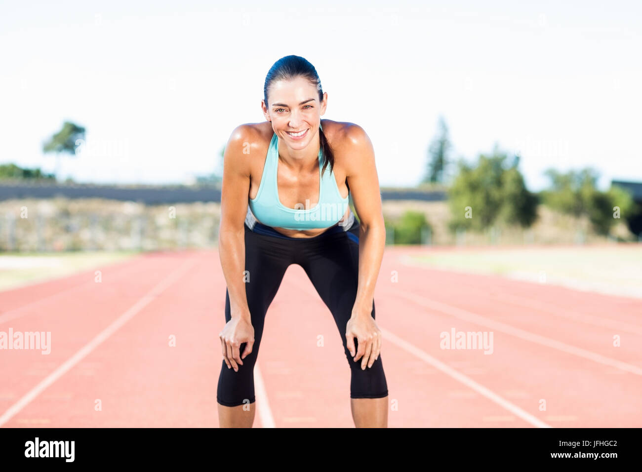 Tired female athlete standing on running track Stock Photo