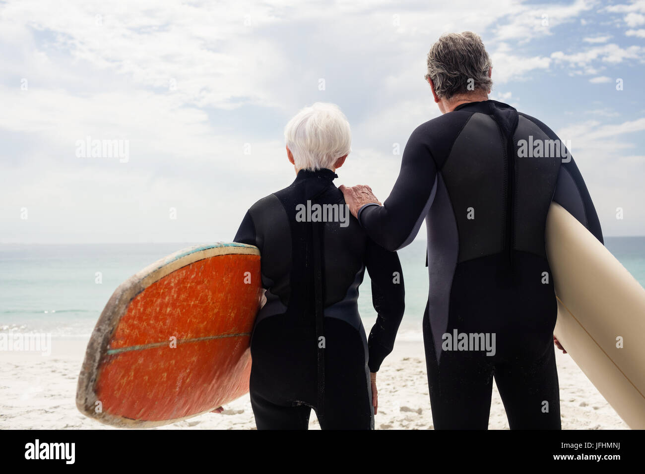 Senior couple in wetsuit holding surfboard on beach Stock Photo
