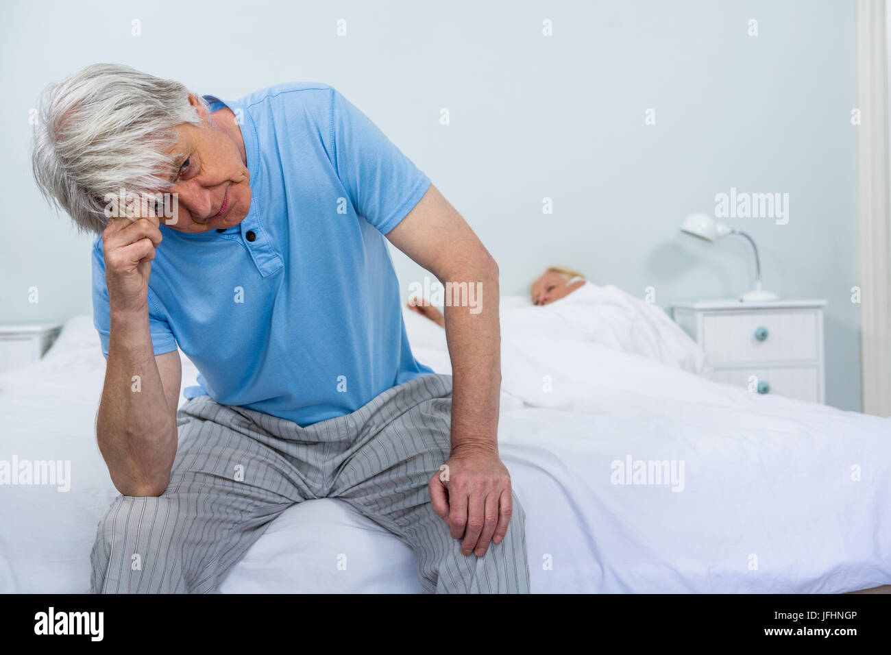 Upset senior man touching head while woman sleeping on bed Stock Photo