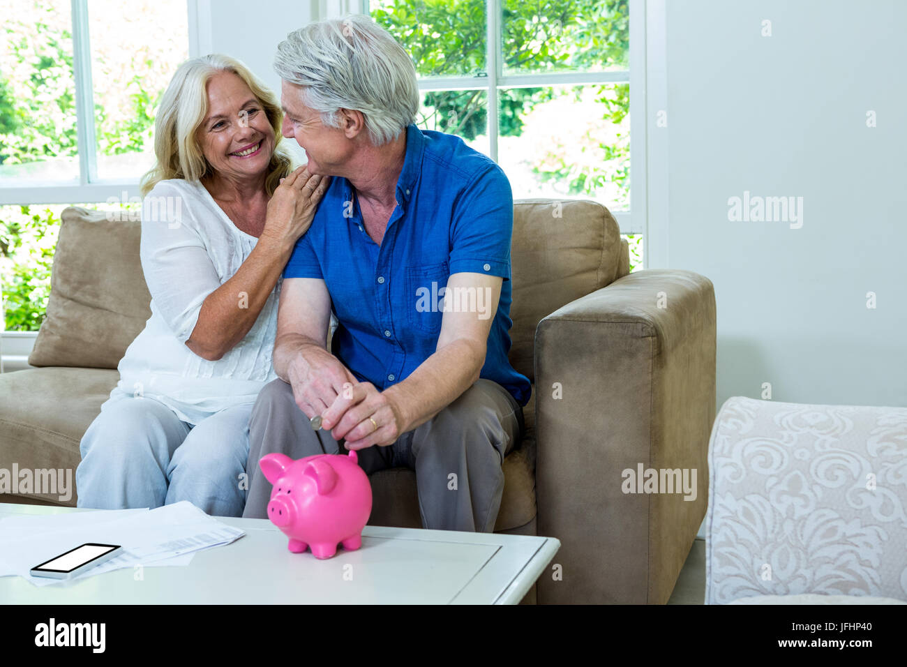 Cheerful senior couple putting coin in piggi bank at home Stock Photo ...