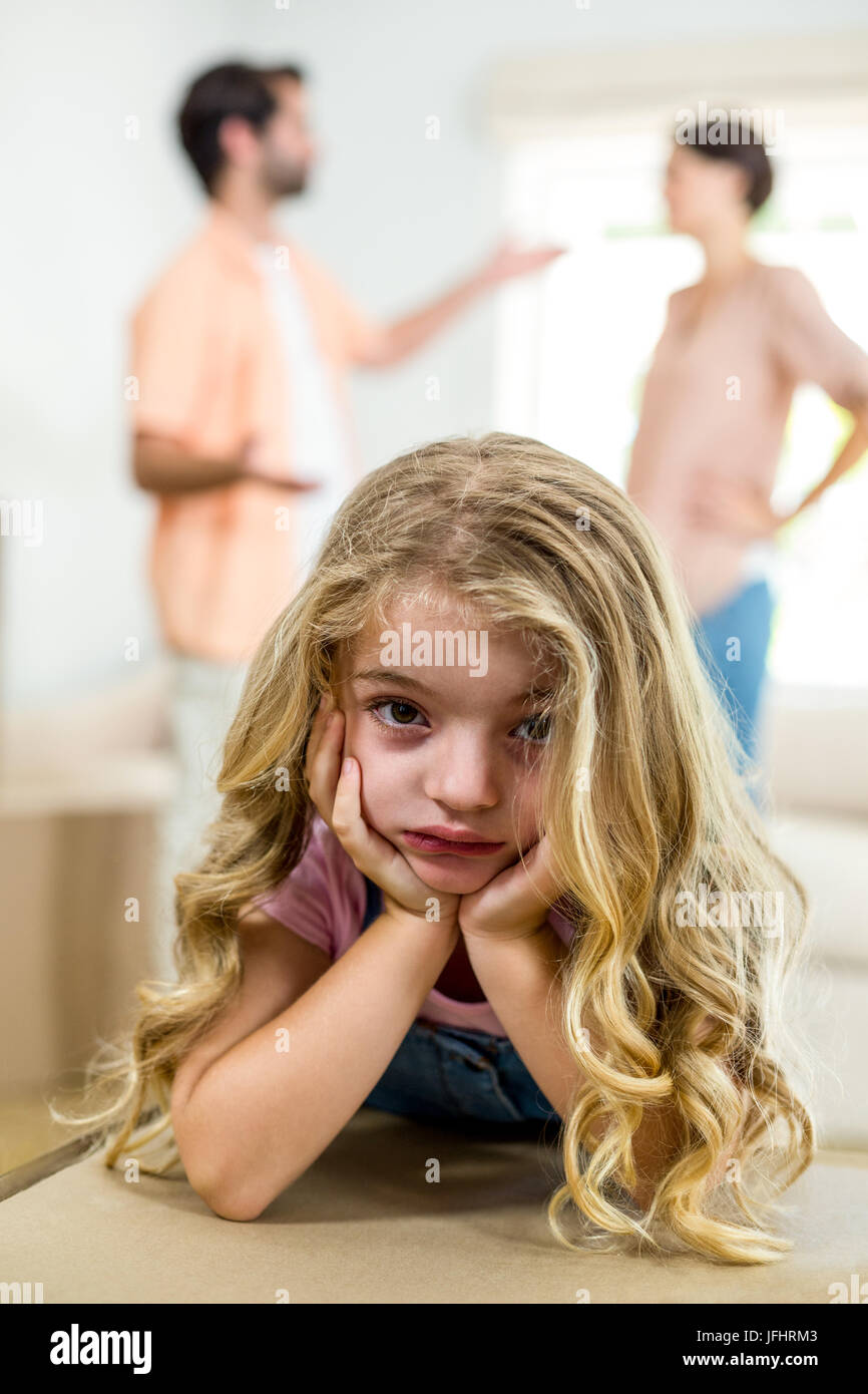 Upset girl leaning on box while parents arguing in background Stock Photo