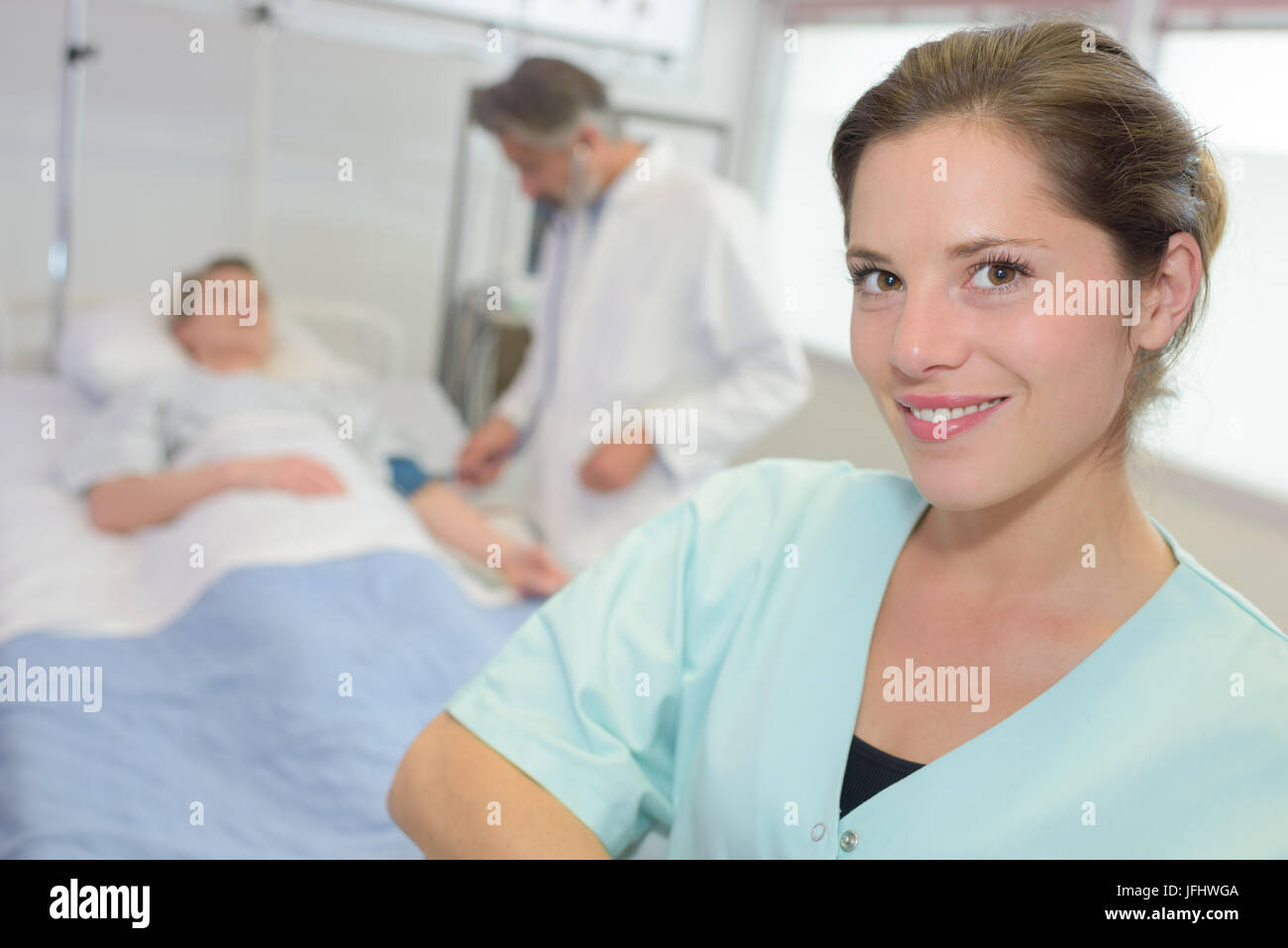 Portrait of nurse, patient in hospital bed in the background Stock Photo
