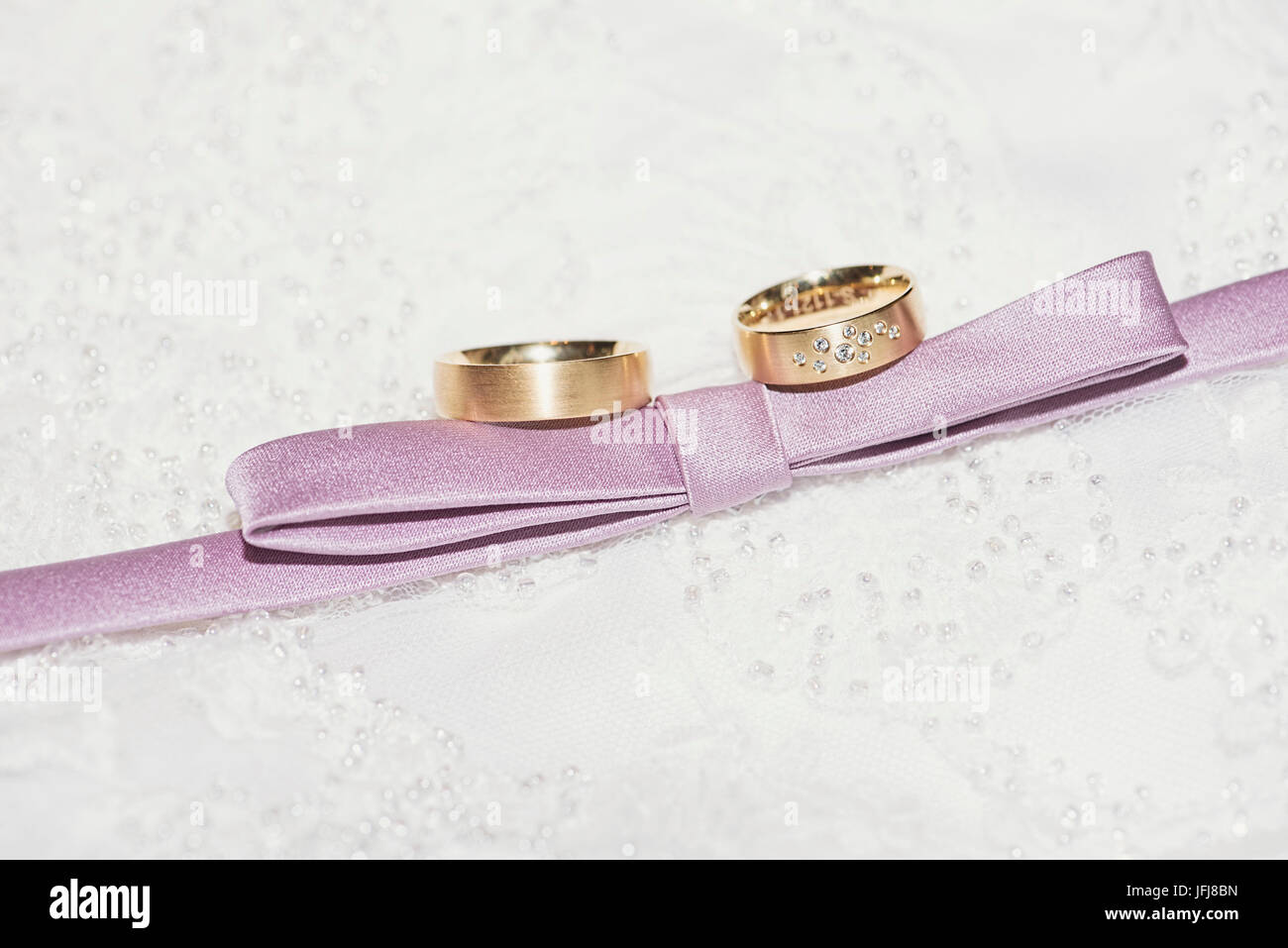 Wedding rings made of gold with diamonds and mauve ribbon on a background made of lacy Stock Photo