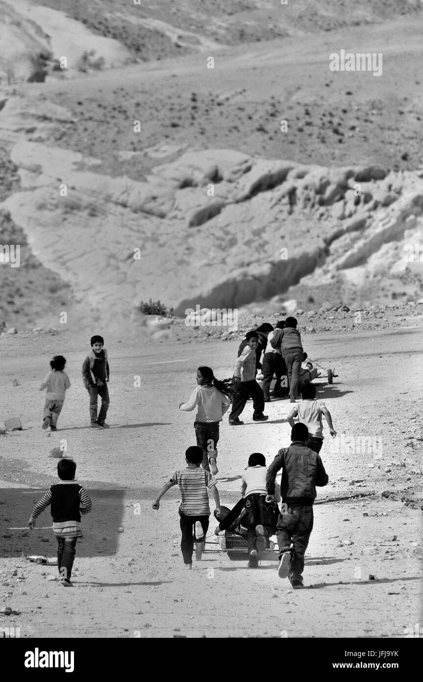 In a road on the outskirts of Petra, some children playing and chasing each other on a dirt road and dusty Stock Photo