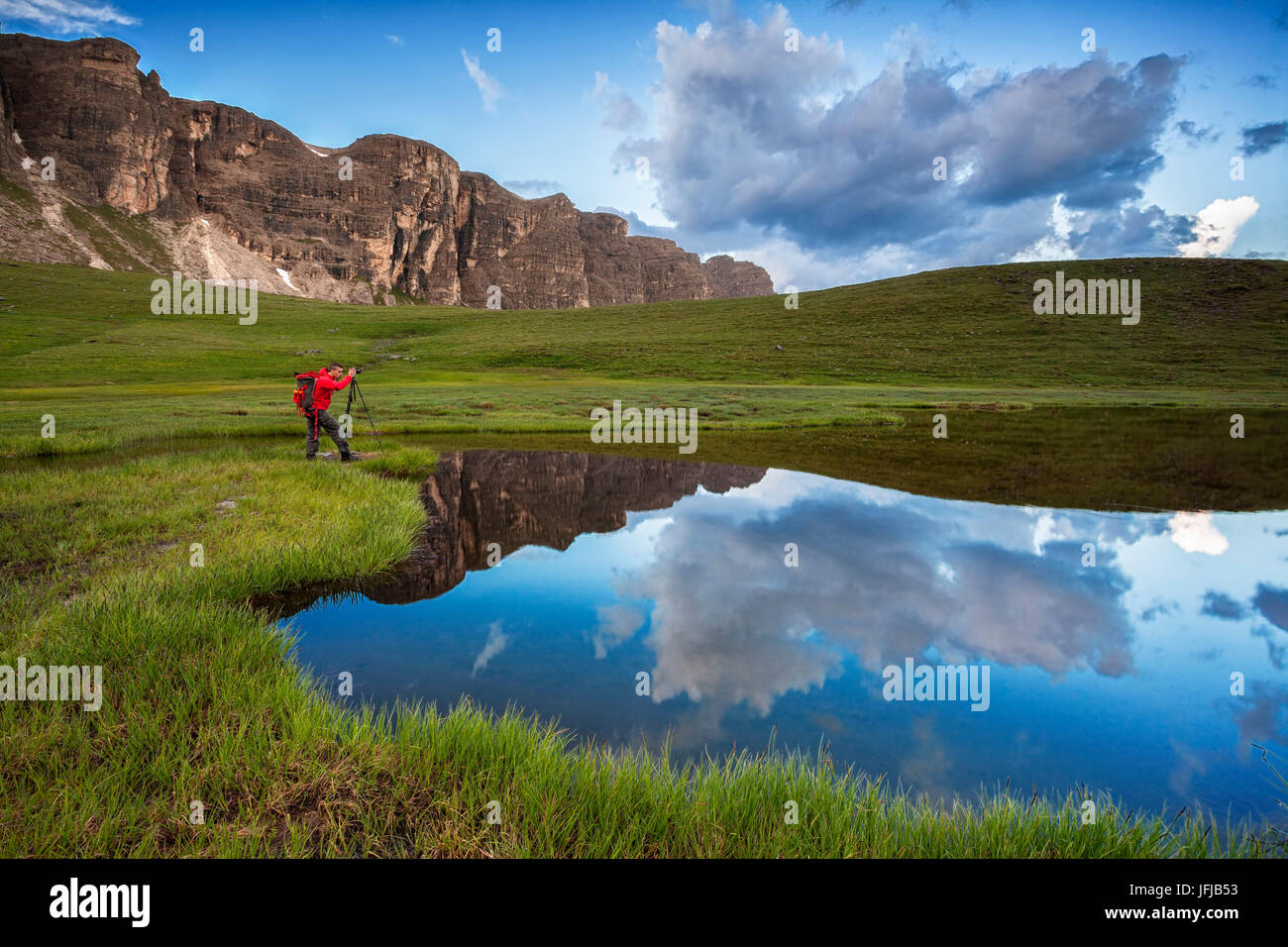 Landscape photographer in action on the green banks of Baste lake, Mondeval, Dolomites, In the background the steep face of the Lastoni di Formin, Veneto, Italy Stock Photo